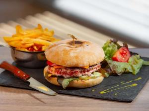 a hamburger and french fries on a plate with a knife at ibis Montélimar Nord in Saulce-sur-Rhône