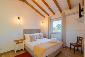 a bedroom with a bed with a window and a chair at Monte do Cerro in Porto Covo