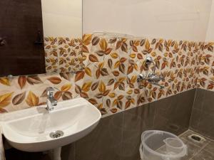 un baño con lavabo y un patrón de hojas en la pared en La Tamara Suite, en Pondicherry