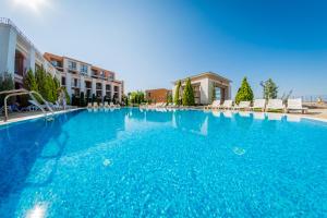 a large blue swimming pool with chairs and buildings at Sea Fort Club Complex in Sveti Vlas