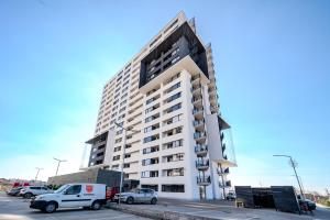 a tall white building with cars parked in a parking lot at Skyline Sunset View -XCity Tower - By OpenHouse apartments in Timişoara