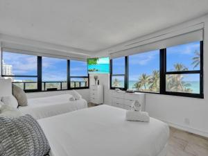 um quarto branco com 2 camas e janelas grandes em Oceanfront Beach Retreat Beach Service 502 em Miami Beach