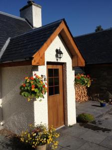 mały dom z drewnianymi drzwiami i kwiatami w obiekcie Drumguish Cottage w mieście Kingussie