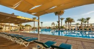 a pool with chaise lounge chairs and palm trees at El Mouradi Port El Kantaoui in Port El Kantaoui