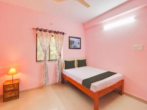 Schlafzimmer mit rosa Wänden, einem Bett und einem Fenster in der Unterkunft Collection O Shadowline Guesthouse in Goa