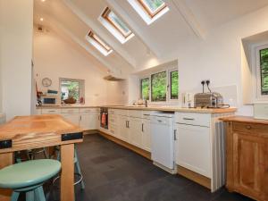 cocina con armarios blancos, mesa y ventanas en Lanvean Farmhouse, en Newquay