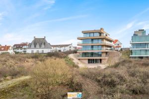 a building on a hill with houses in the background at Rêve des Dunes – luxury apartment by the sea in Koksijde