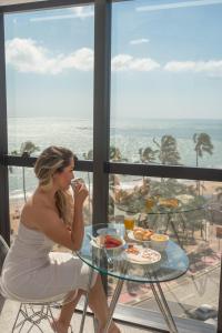 una mujer está sentada en una mesa comiendo comida en Hotel Brisa Tower Maceió, en Maceió