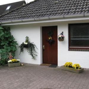 a white house with a brown door and some flowers at Fewo Leopold - Ferienwohnung 1 in Cuxhaven