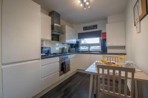 uma cozinha com armários brancos e uma mesa com bebidas em Park View-modern 2 bed apartment em Motherwell