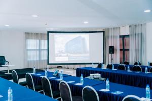 Beira Terrace Hotel في بيرا: قاعة اجتماعات ذات طاولات وكراسي زرقاء وشاشة