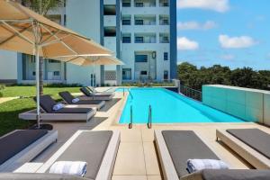 a swimming pool with lounge chairs and an umbrella at Entire luxury 2 bedroom en-suite apartment at Regency Hotel in Pretoria