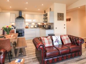 a living room with a leather couch and a kitchen at Pine Marten in Dornoch