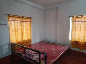 Cette petite chambre comprend un lit et deux fenêtres. dans l'établissement SHANTINIR HOMESTAy, à Santiniketan