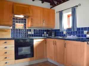 a kitchen with wooden cabinets and a black dishwasher at Byre Cottage - Meadowbrook Farm in Thame