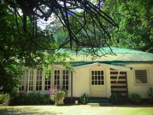 ein kleines weißes Haus mit einer Veranda und Bäumen in der Unterkunft Surrey Bird Sanctuary & Holiday Resort in Welimada