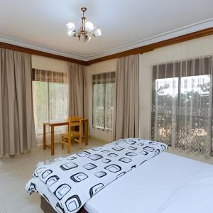 1 dormitorio con cama, mesa y ventanas en Maison De Omashi, en Kigali
