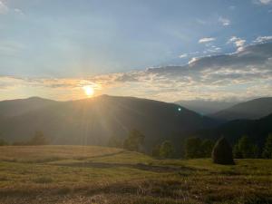 a sunset over a field with the sun setting on a mountain at Casutele din Poienita in Comarnic