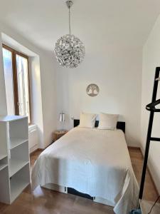 Habitación blanca con cama y lámpara de araña. en Appartement de charme avec balcon au pied des commerces en Béziers