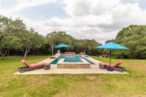 a swimming pool with two umbrellas and chairs at Get Back to Nature at Secluded Hill Country Oasis in Driftwood