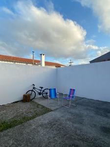 zwei Stühle und ein Fahrrad stehen neben einer weißen Wand. in der Unterkunft Casa em Condomínio Fechado in Pelotas