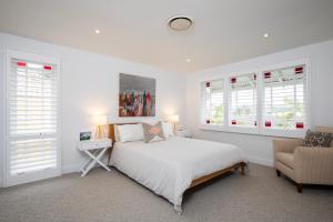 ein weißes Schlafzimmer mit einem Bett und einem Stuhl in der Unterkunft Seaside apartment, 100m to beach in Narrabeen