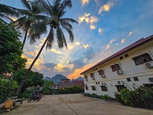 a palm tree in front of a building with a sunset at Saphaothong guesthouse in Vang Vieng