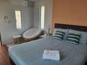 a bedroom with a large bed and a chair at Homlomchomsuan หอมลมชมสวน in Ban Mai