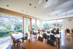 un restaurante con mesas, sillas y ventanas grandes en Shiki Resort Atami Boyokan, en Atami