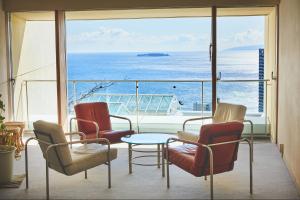 a balcony with chairs and a table and a view of the ocean at Shiki Resort Atami Boyokan in Atami
