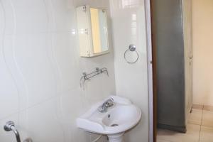 a white bathroom with a sink and a mirror at Rashmi Cottage in Dagshai