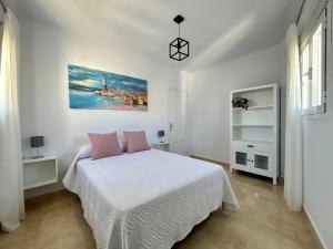 a white bedroom with a bed with pink pillows at Apartamento Alto Castillo, centro histórico con garaje y WiFi in Sanlúcar de Barrameda