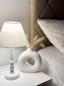Danin apartmani في بار: مزهرية بيضاء بجانب مصباح على سرير