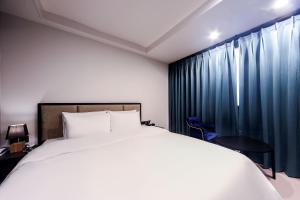 - une chambre avec un lit blanc et des rideaux bleus dans l'établissement ON:NA Hotel, à Busan