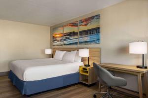 a hotel room with a bed and a desk with a chair at Days Inn by Wyndham Cocoa Beach Port Canaveral in Cocoa Beach