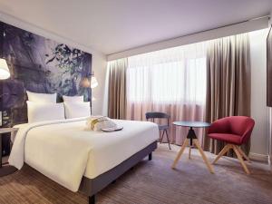 Cette chambre d'hôtel comprend un grand lit et un fauteuil rouge. dans l'établissement Mercure Paris La Défense, à Courbevoie