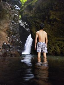 a man standing in the water in front of a waterfall at Goa Walet Cottage in Praya