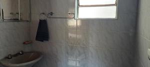 a white bathroom with a sink and a window at Suíte Com Estacionamento Perto do Centro in Campos do Jordão