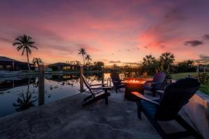 um pôr-do-sol sobre uma piscina com cadeiras e uma mesa em CapeCoral Waterfront Villa - Heated Pool & Jacuzzi em Cape Coral