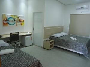a room with two beds and a desk and a chair at Hotel Jequitibá in Gurupi