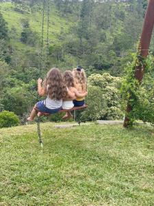 three girls sitting on a swing in a field at Refúgio nascer das águas in Gravatal
