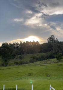 a field with a fence and the sun in the background at Refúgio nascer das águas in Gravatal