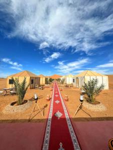 a red road in the middle of a desert with tents at Sahara Desert Camp in Adrouine