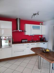 une cuisine avec des placards blancs et un mur rouge dans l'établissement Maison Guidel Plages 4 à 8 personnes, à Guidel