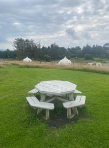 una mesa de picnic y dos bancos en un campo con tiendas de campaña en Seascape Belle Tent - 2 Person Luxury Glamping Belle Tent en Dungarvan