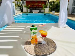 a drink and a glass of orange juice next to a pool at KEUR MATY Charmante et Moderne Villa 5 chambres, 5 salles de bains à Warang in Ouoran