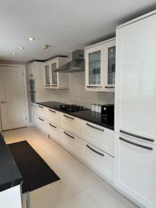 Brentford Guest Rooms في برينتفورد: مطبخ مع خزائن بيضاء وقمم منضدة سوداء