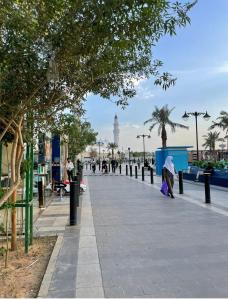 a woman walking down a sidewalk with a clock tower in the background at شقة مخدومه مفروشة قباء 303 in Al Madinah