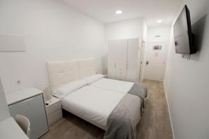 a white bedroom with a bed and a tv at Pension MD in San Sebastián