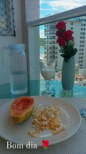 un plato de comida en una mesa con un jarrón con flores en Apart° Grande Lar en Guarapari